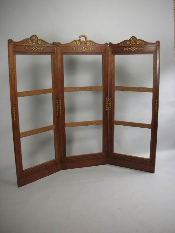 Empire style walnut three panel screen, each panel double hinged and decorated with carved and giltwood neoclassical devices; the center with a wreath; the side panels with anthemions.