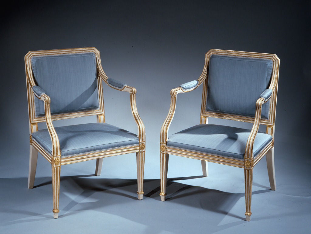 A fine pair of painted and parcel gilt open armchairs in the French taste with upholstered square moulded backs and seats, the back having fluted rails, scrolled arms and square tapering legs headed by paterae. Modern silk upholstery