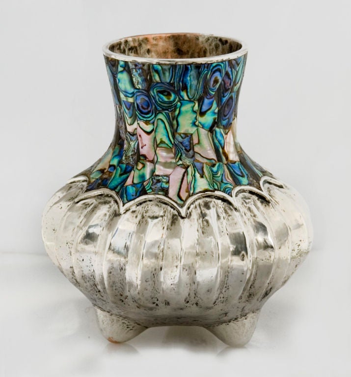 
A fine vase by Los Castillo, of Mexico, the neck embedded with multi-colored abalone, the body of ribbed, melon form, all on three (3) feet.  Dimensions:  5 7/8 inches tall by 5 1/2 inches across lower body of vase.  

No monogram. Marked as