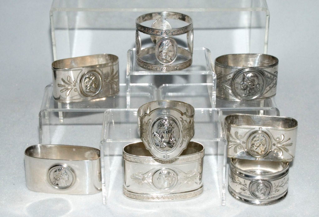 A fine set of eight (8) circa 1875 coin silver and silverplate napkin rings by varied makers, all in the medallion motif.  The napkin ring at the base of the lead pictures is manufactured by Wood & Hughes and is coin silver, all others are