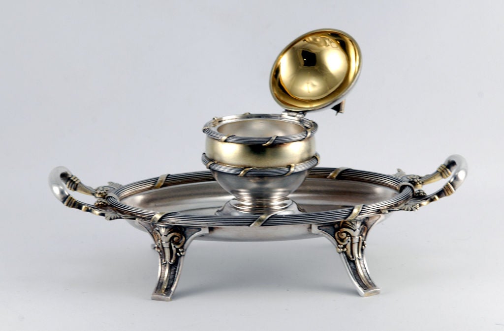 A fine circa 1873 sterling silver inkwell on stand by Gorham of Providence, RI, the stand and ink container with applied 'ribbons, in the aesthetic taste, the ribbon at top of well becoming a pen, with 2 applied handles, all on four (4) curved feet,
