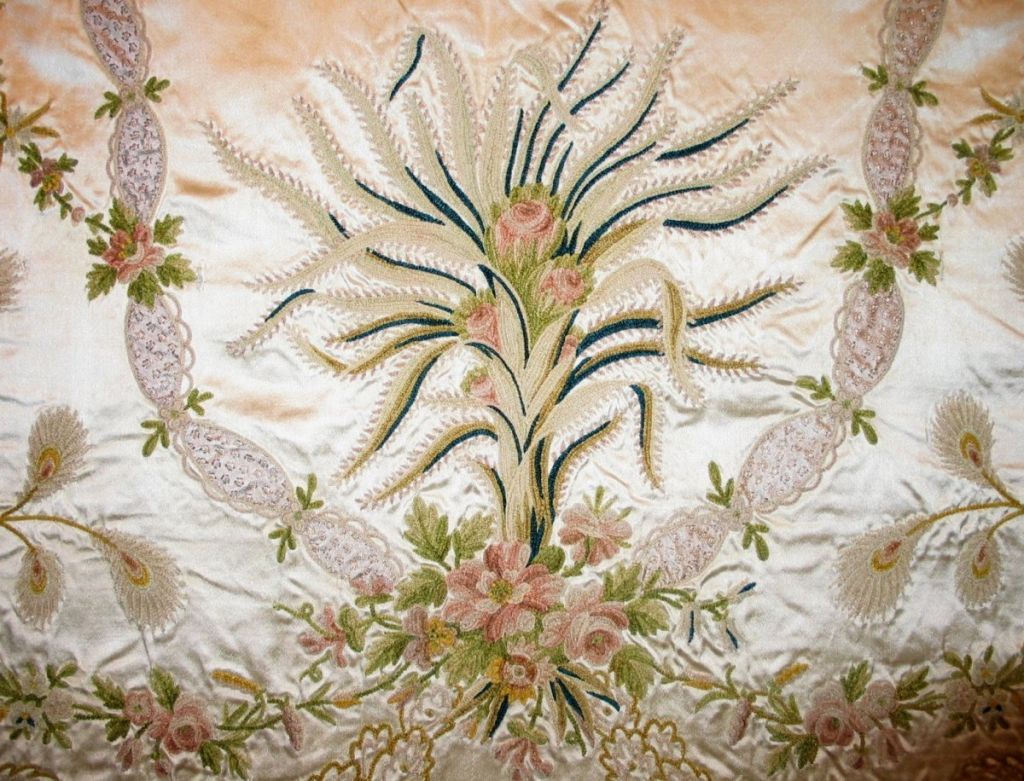 18th C. French chenille embroidered panel on a silk satin ground with a central floral design surrounded by lace and leaf swags with flowers.