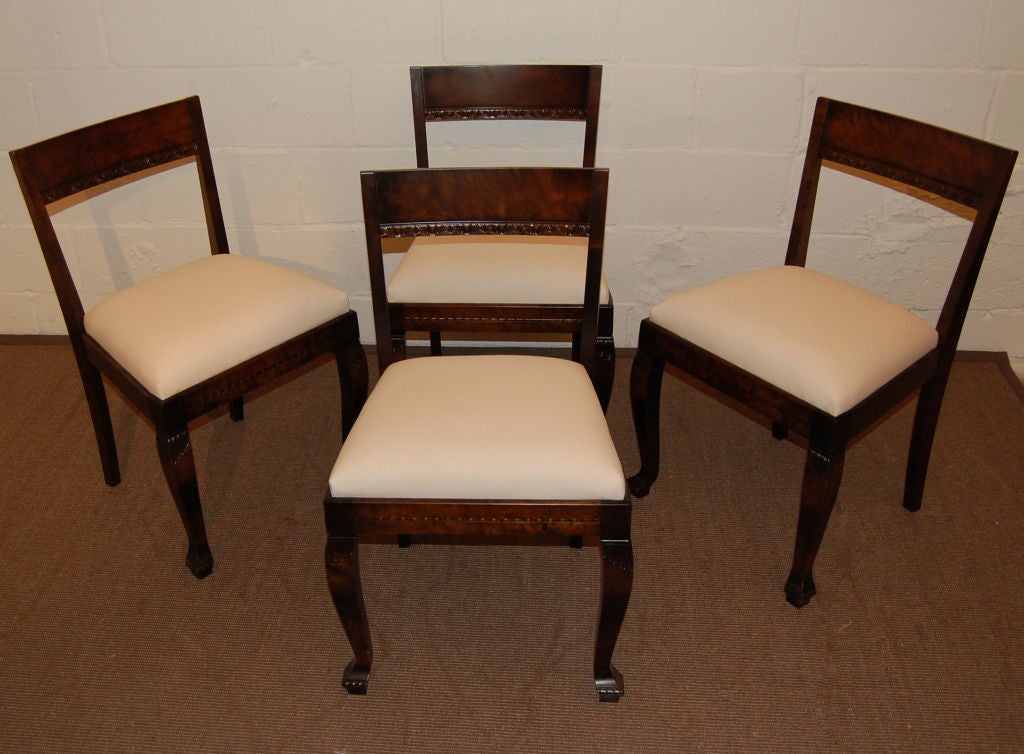Set of four carved Art Deco neoclassical style dining chairs in dark flame birch from c. 1930's Sweden.  Seats have been newly rebuilt, padded and covered in ivory duck cloth - and are ready for your COM fabric.  

Cost of reupholstery is