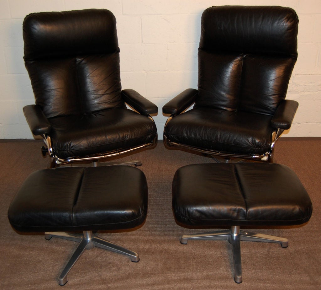 Pair of Swedish Modern black leather and chrome adjustable lounge armchairs with matching ottomans.  On chrome swivel bases, these vintage chairs are in great shape, recline and adjust and are very comfortable.  Designed by