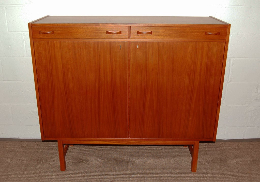 Slim teak server/buffet by Ulferts of Tibro, Sweden. Two dove-tailed top drawers, one divided and lined with green felt for flatware. Locking cabinet doors reveal a golden birch interior with white melamine shelves and back. Key