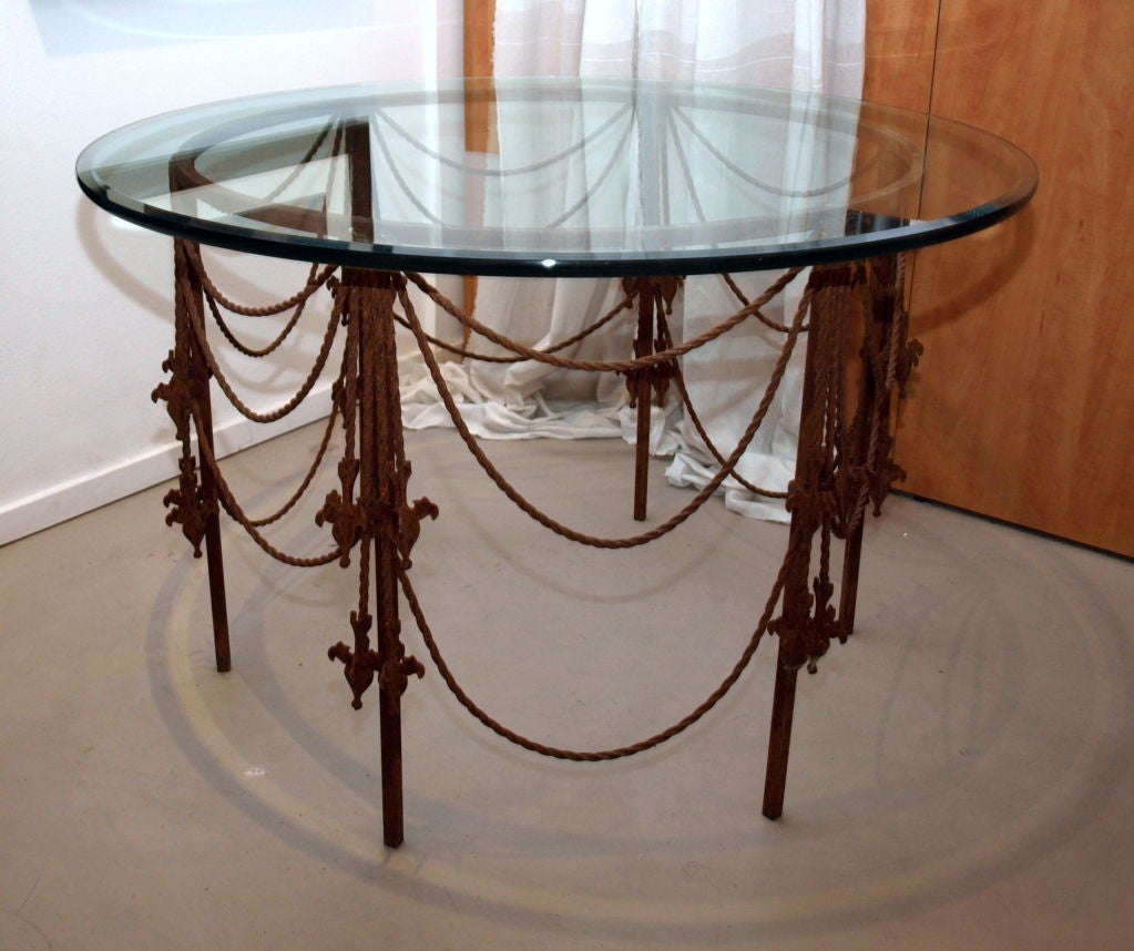 The swag design in this table comes from the 1920’s era, however, usually seen in the form of fabric covering a window or a table.   Each swag is made of twisted wrought iron and there are metal tassels that accent the ends of each swag.<br />
<br