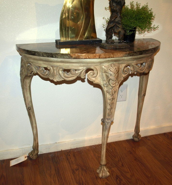 This Demilune console table of carved wood has rich earth tones, claw feet, a gargoyle, hand-carved shells and scrolls, together with a faux marble top that would take a mineral expert to point out the difference from it being real marble.  Wherever