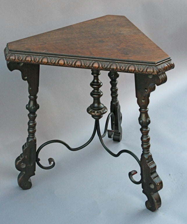 Nicely carved 1920's Spanish Revival table in an unusual triangular or corner shape.  Features include wrought iron stretcher, turned legs, and burled wood top.