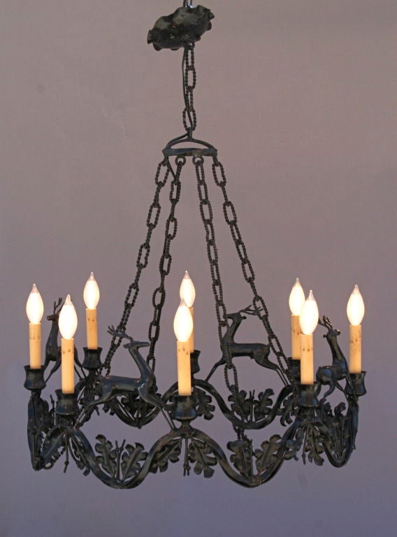 Whimsical vintage chandelier of wrought iron featuring stylized prancing deer above oak leaf garland. Eight candle-style lights.