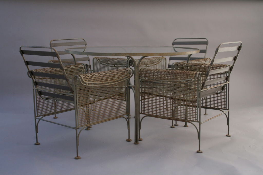 Finely designed Woodard patio set featuring Machine Age design reminiscent of the German Bauhaus tradition.  The chairs are styled with wire mesh siding and rolled arms on a heavy iron frame.  Sharply defined table with simple lines.  Quality