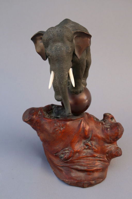 A finely detailed elephant gracefully balancing atop a ball.  The piece was made in Japan in the early part of the 20th century and is signed with chop mark.  The base is made of polished burled cherry wood.   The surface is richly detailed with