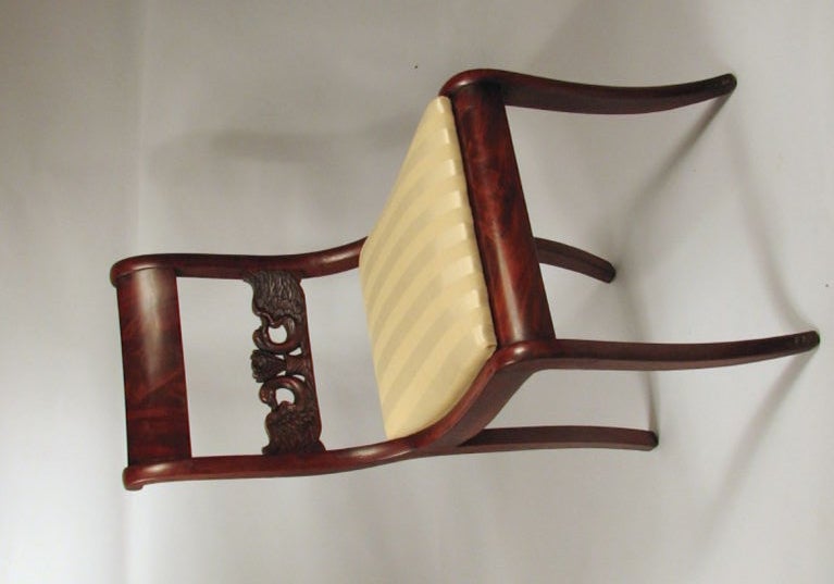Pair of neoclassical carved mahogany side chairs, with curved figured mahogany crests above facing swan carved horizontal splats, with curved stiles framing slip out seats raised on sabre front and raking rear legs. Probably continental, early 19th