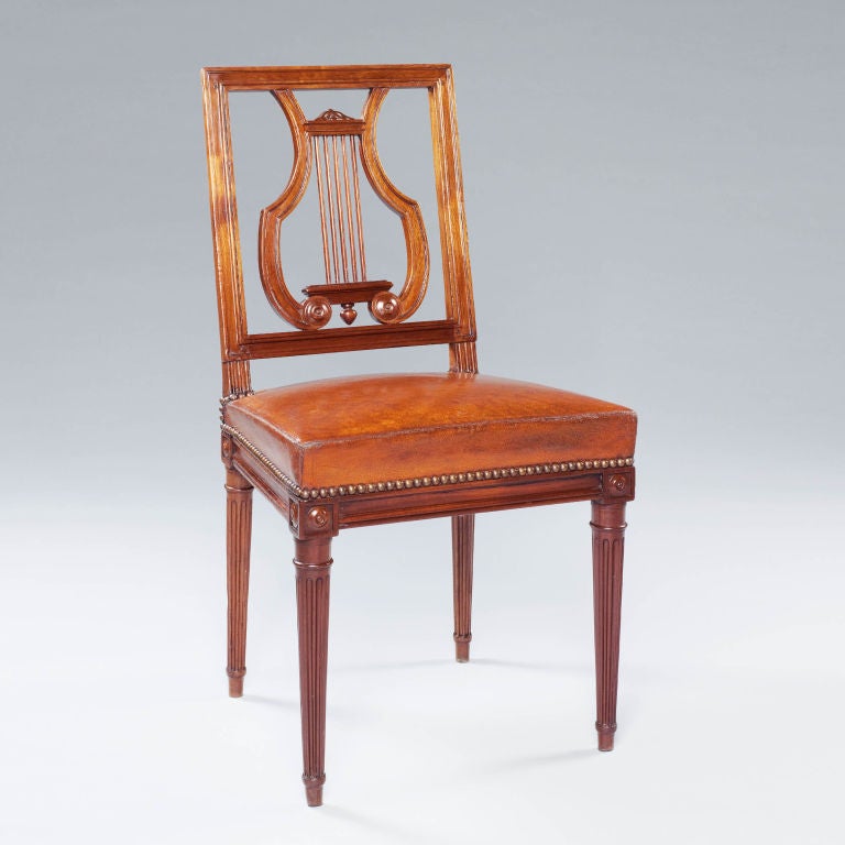 An unusual set of twelve mahogany lyre back Louis XVI dining chairs. Each chair precisely carved with a rectangular back with central splat carved in the form of a lyre. The square seats are set with paterae on the corners above turned tapering