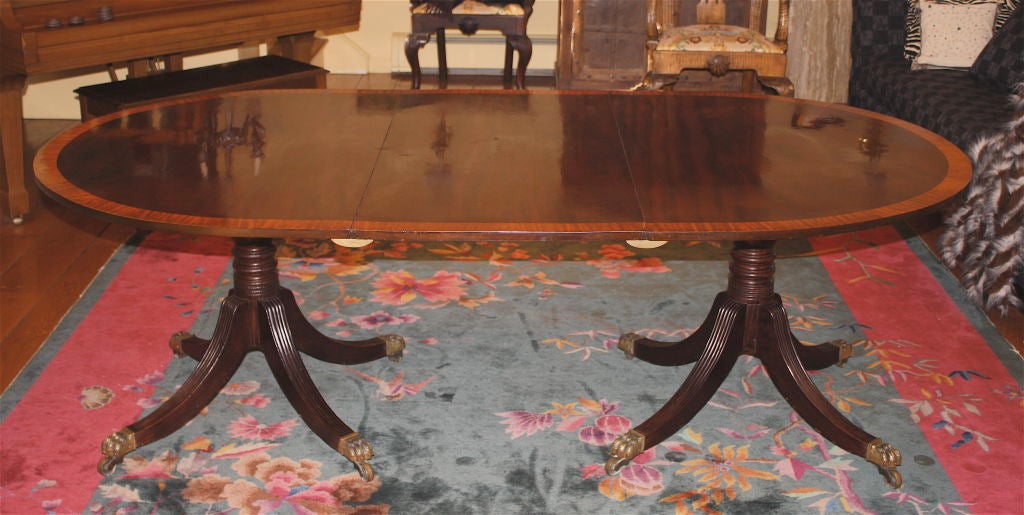 A highly polished vividly grained dark mahogany, with sharply contrasting satin birch cross-banding; double pedestal dining table.  The demilune pedestal sections retain their original <br />
brass tilt top mechanisms.  The pedestals are boldly
