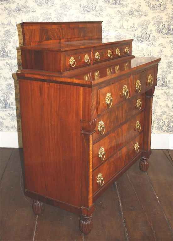 To the 'Egyptian Taste', an 8 drawer stepback chest or bureau, with multiple contrasting crotch and flame mahogany veneers and banding. Acanthus leaf capitals top the birds eye maple obelisk columnar insets; raised on four inverted acanthus bulb