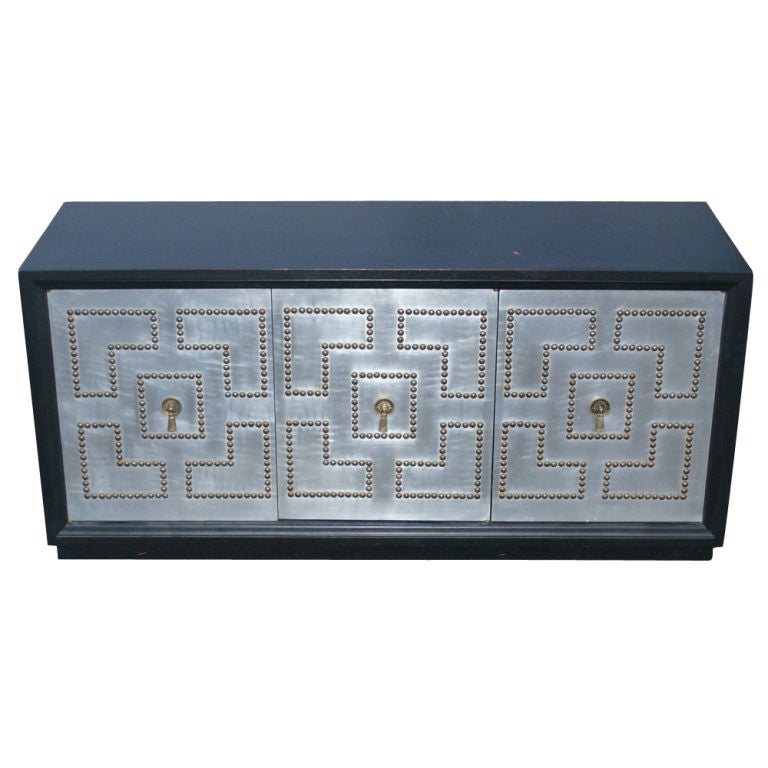 Ebonized wood cabinet construction with 3 cabinet doors and interior shelves.
Doors with stainless fronts and studded in a geometric pattern with tassel pulls.

 