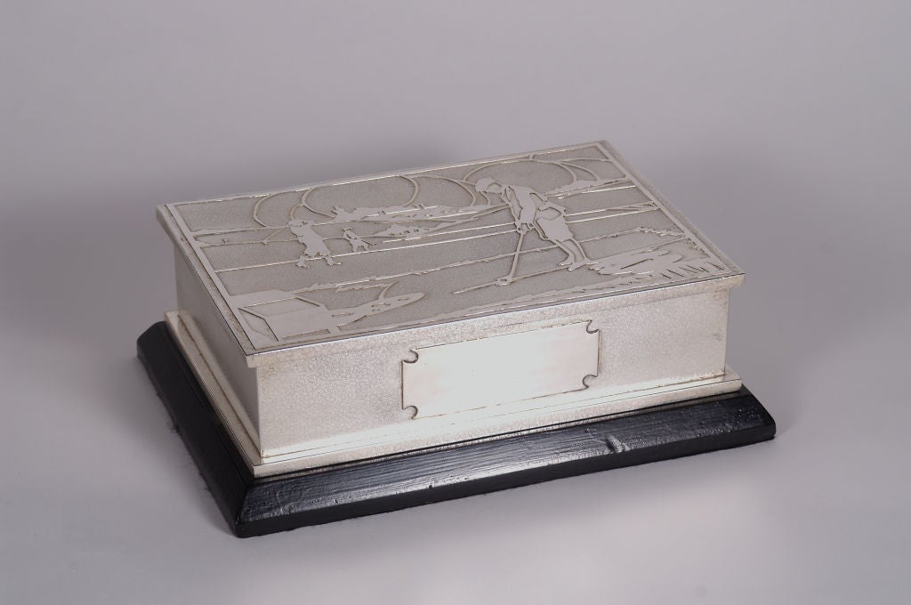 An unusual and stylish silver plated cigar box on an ebonised base, the lid featuring an Art Deco scene of a golfer on the fairway, about to take a putt, the cedar lined interior with central divider, and a vacant cartouche to the front.