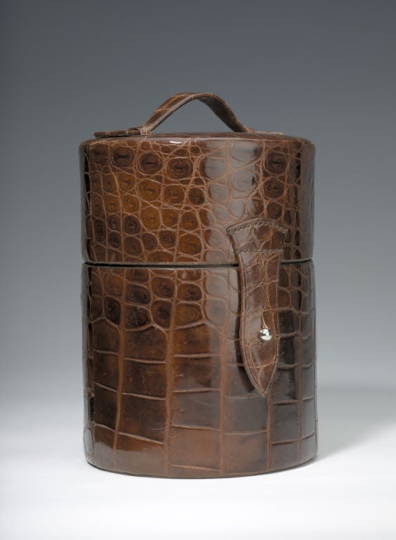 A magnificent and very rare crocodile-skin travelling bar of cylindrical form, the top opening to reveal various silverplated fittings, including three curved flasks marked ‘GIN’, ‘FRENCH’ and ‘ITALIAN’, surrounding a centrally-mounted cocktail
