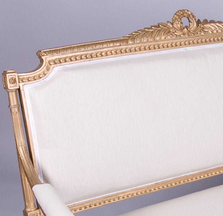 This very elegant gilt wood Louis XVI Style Settee is upholstered with muslin fabric. The gilt wood frame has fluted legs with acanthus leaves motifs. The top rail has a beautiful carving of laurel leaves and a wreath.