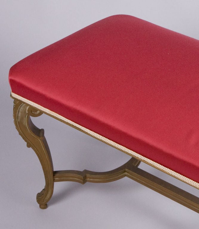 This Louis XV Style Bench from Provence is made of painted maple wood.  The cabriole legs have acanthus leaf motifs and an H-shaped stretcher. The seat is upholstered in red fabric.