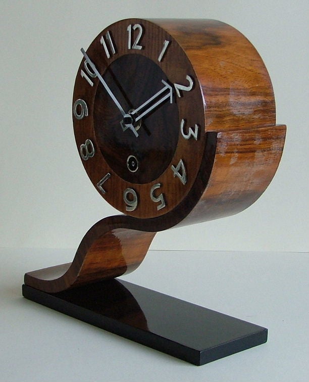 This is a fantastic clock with a great streamline design , veneered in figured walnut and satin birch with a black lacquered base , silvered bronze numerals and silver lacquered brass hands. This is quite an unusual design and a clock I have never