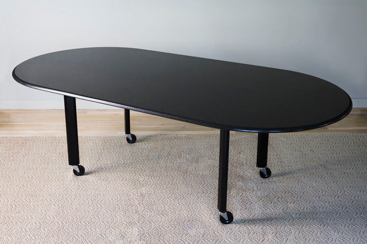 Black granite top racetrack table on black steel oval legs mounted on castors.