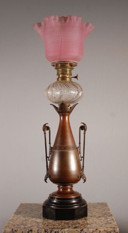 Pair of lamps with bronze vase and cast handles, mounted on black marble base.  Pressed, clear glass fluid container.  Pink striped original glass shade.