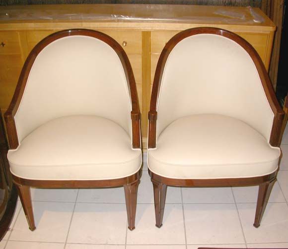 A pair of chairs attributed to Lucien Rollin with stained walnut frames, cut edged angled legs with carved sabots, frames and skirt band, open grooved column arm fronts newly upholstered with ivory leather.