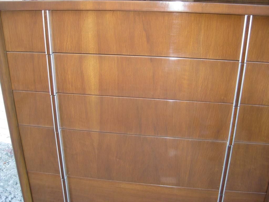 John Widdicomb signed highboy six graduating drawers, with flat racetrack oval legs gives a unique look to this Mid-Century, modernist design dresser with bookmatched grain pattern and banding on top and vertical pulls. This item is on sale for a