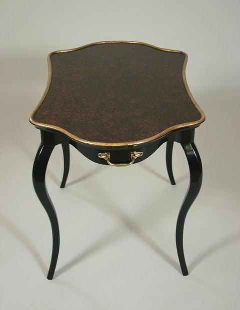 A late 19th century shaped black lacquer table

with a silver gilt border and faux painted top.