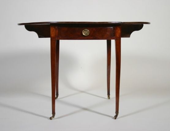 An American late 18th century oval mahogany pembroke table.

The finely grained top above a single bowfronted drawer flanked by paterae with inlays in satinwood, poplar and ebony, all raised on square tapering legs ending in brass castors.