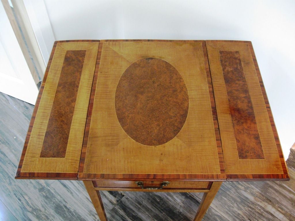 An English late 18th century harewood pembroke or writing table; the burl yew wood oval inlaid and rosewood cross banded top flanked by two drop leaves with rectangular burl yew wood inlay and rosewood cross banding above a single drawer similarly