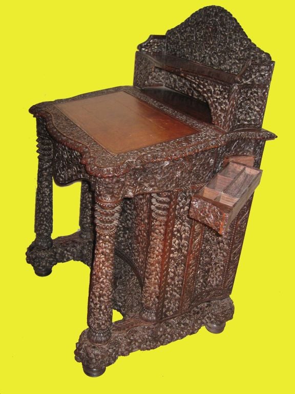 Anglo-Indian carved with animal and vegetal motifs teak davenport desk, carved gallery on shelf surmounting the leather topped writing slope, with four interior drawers; the body is raised on two front columns,backed by carved case holding pen