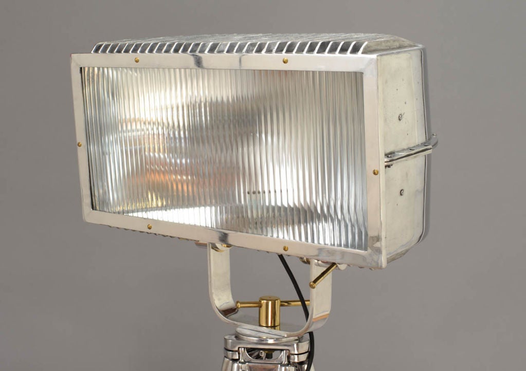 A polished constuction light with a curved mirrored rear reflector. The ridged top and bottom give this light it's distingished look.  The tripod has been refinished to a handsome walnut color.  The details and fittings are solid brass.
