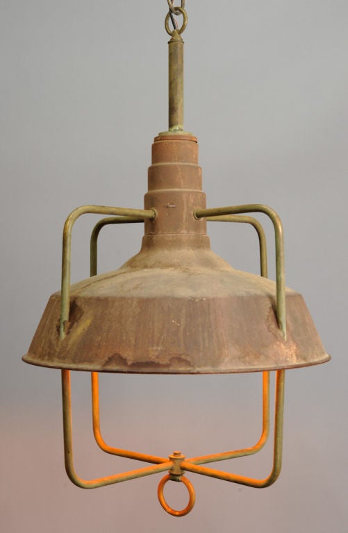 A pair of industrial lights are the 1940's with wonderful age and patina.  The shade and cage intersect to a at a brass ring and tappered top.  They have been rewired for standard bulbs from 5 to 200 watts.  The insutrial wear it wonderful.  Priced