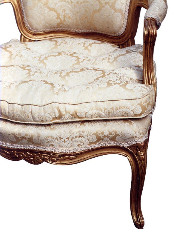 A pair of comfortable exemplary French Rococo armchairs/bergeres (fauteuils a la reine). Gilt wood frames with car-touche-shaped padded seat backs, padded arms, serpentine rails and cabriole legs. Fine foliate wood-carvings, loose cushion over
