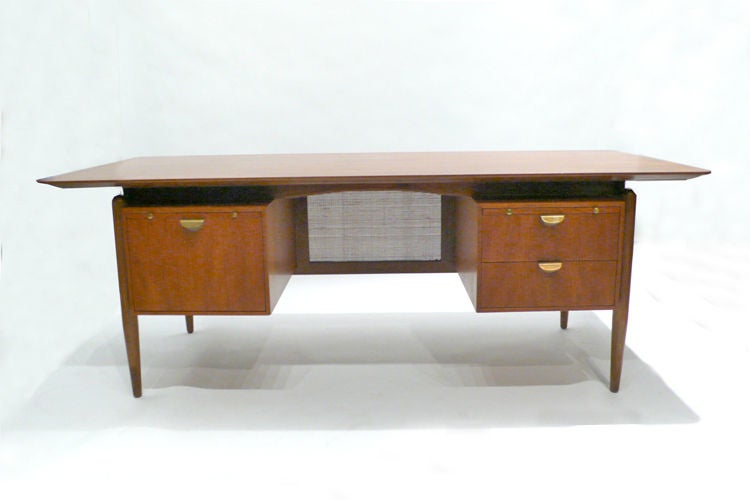 Large Scale desk designed by Finn Juhl for Baker, 1950s with cane modesty panel, brass pull, two pull out writing surfaces, pencil drawer with original paperclip tray, file and storage drawers.