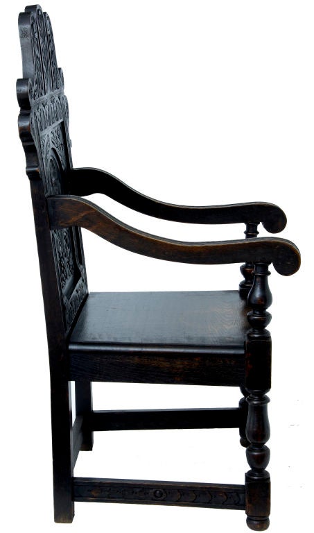Victorian carved oak wainscot armchair with carved scoll cresting above carved panel back and standing on carved cup and cover front legs.