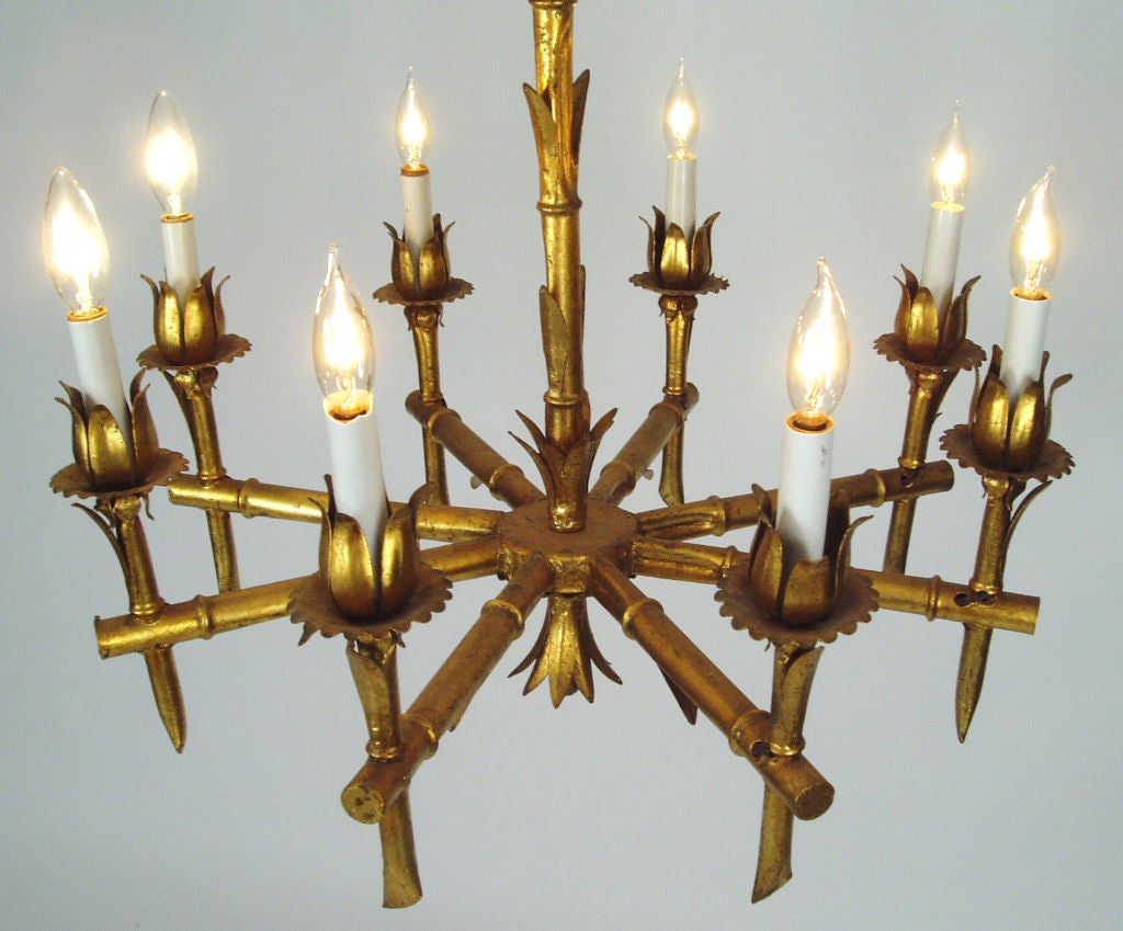 a stunning 8 light mid-20th century faux bamboo gold leaf chandelier. perfect form with each straight arm holding a vertical tapered light with bamboo motif all over and leaves scattered as well. excellent patina on the gold leaf. absolutley