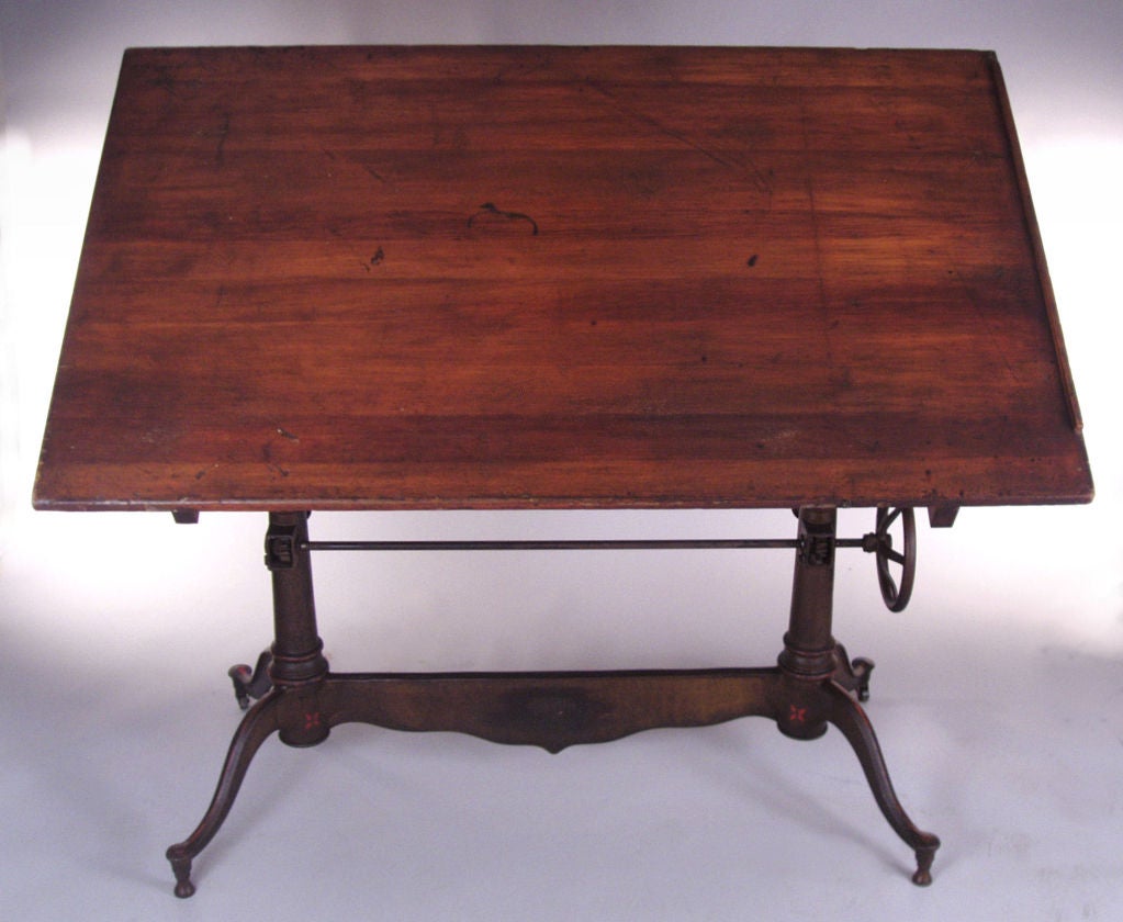 an outstanding antique early 20th century drafting table by Dietzgen. This is one of their most impressive tables, with an elaborate cast iron base with a curved and scrolled center section, and legs at either end. the top is adjustable in angle and