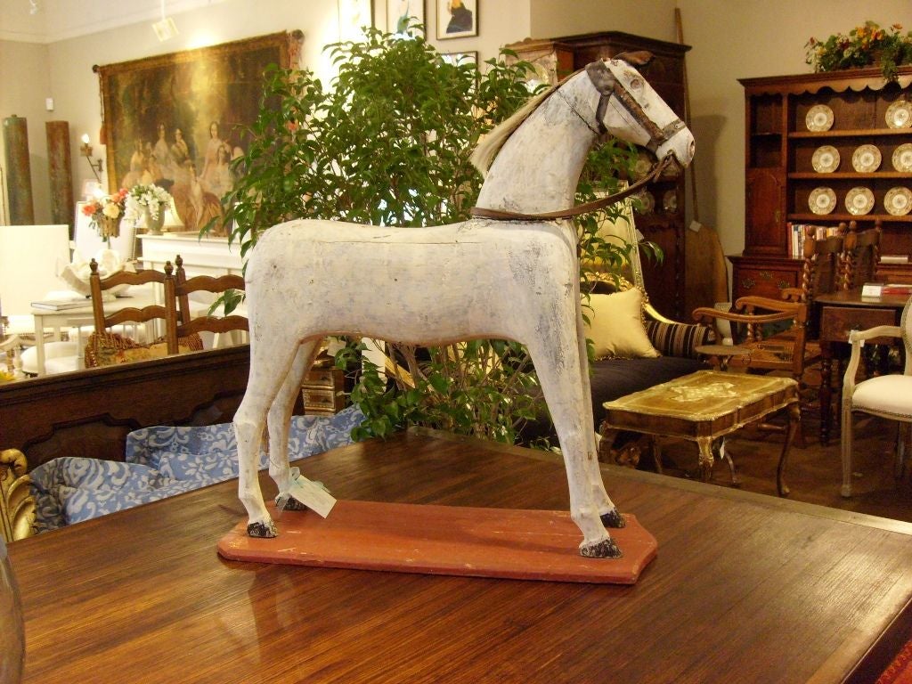 Painted wooden white horse with glass eye, leather tether, twine tail.