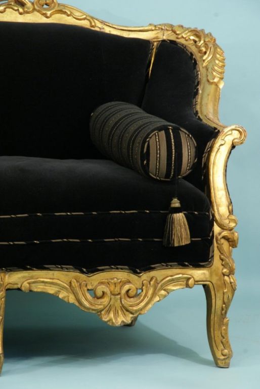 Elaborately carved wood frame settee gilded and upholstered in luxurious black mohair.  2 tasseled roll pillows