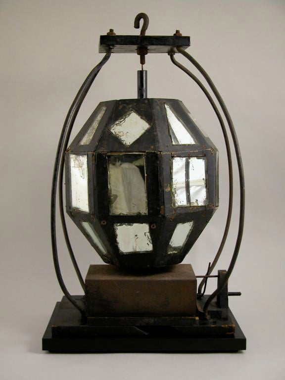 Mechanical mirrored ball.

Mirror set into hollow faceted form of blackened wood and plaster atop a 

clockwork can. Attached to wood base, curving iron struts support vertical rotation,
New York, circa 1900-1940.