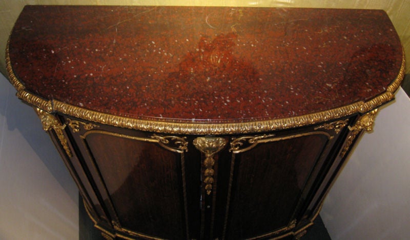 This Louis XVI style meuble a hauteur d' appui has a warm, reddish brown patina, and is crafted from mahogany with rosewood or kingwood. It features a rouge marble top, crosshatch parquetry inlay, and neoclassical gilt bronze mounts including lion