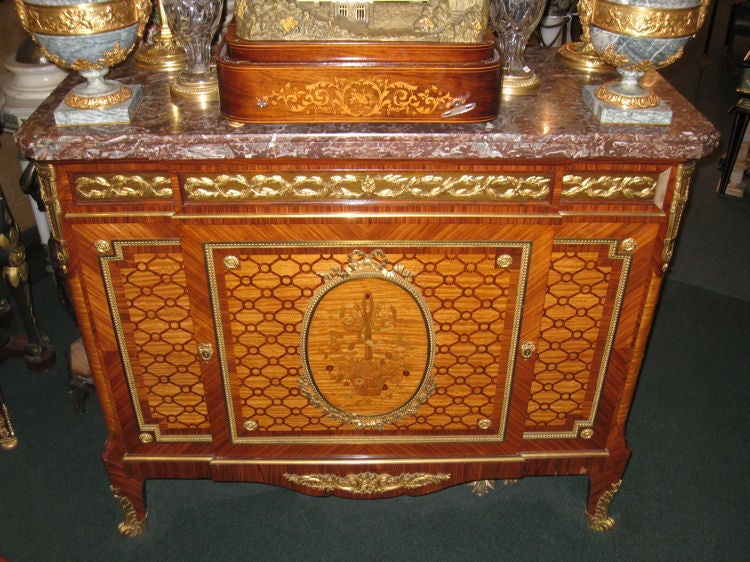 This antique rosewood and satinwood side cabinet in the French Louis XVI style dates from circa 1900, and features exceptional doré bronze mounts, geometric parquetry inlay, and a centre door with flower basket marquetry inlay. It measures 53