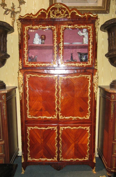 This unique cabinet in the French, Louis XV manner dates from the early 19th century and features two sets of doors with quartered-rosewood veneer and a glazed upper cabinet, and extensive ormolu bronze garland mounts with Greek masks at the