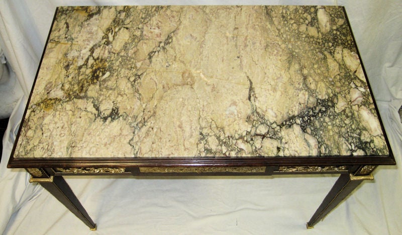 This antique center table in the French Louis Xvi style dates from the late nineteenth century. It features a variegated marble top and extensive gilt bronze mounts along the frieze, legs and feet. The frieze is decorated with bronze foliate