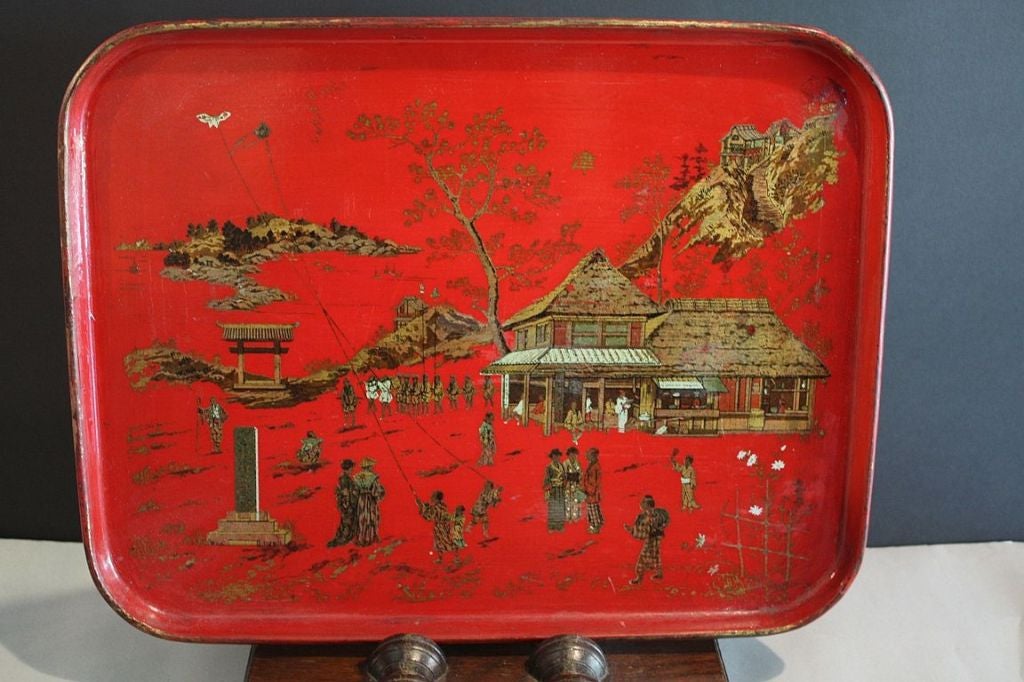 A red lacquered papier mâché tray from England, featuring a Chinoiserie transfer design of a village scene with a pagoda and children flying kites in gold and white.