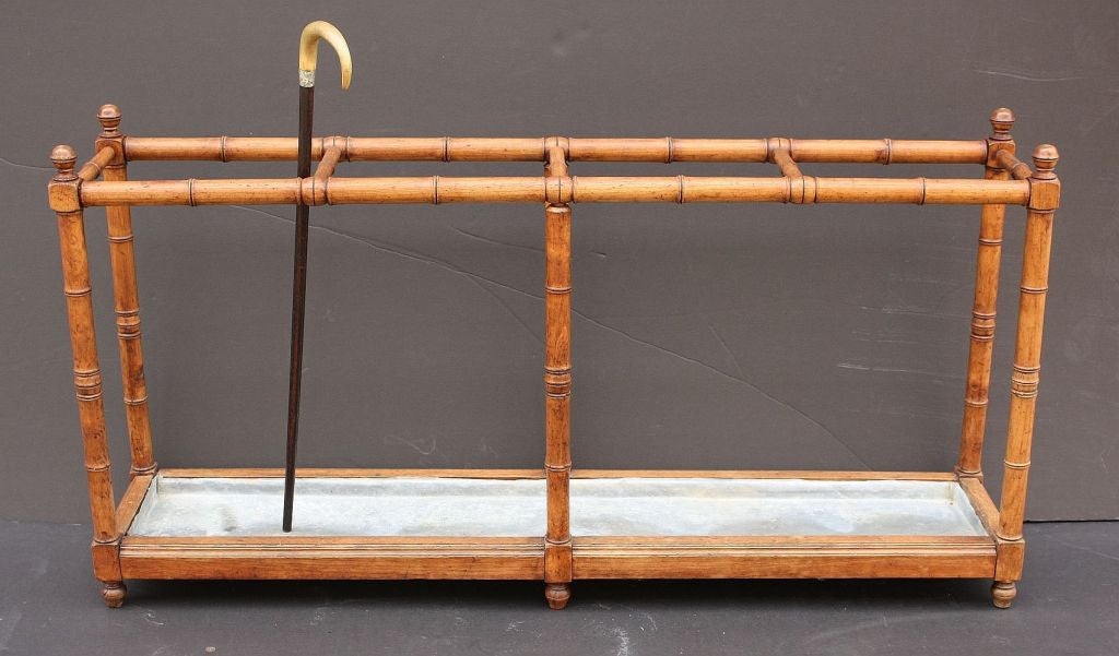 A handsome large Faux Bamboo umbrella or stick stand featuring a turned wood railing and supports with a bamboo design, embellished with spherical turned finials and turned feet. With a fitted tin liner at the base.

Pictured walking cane not