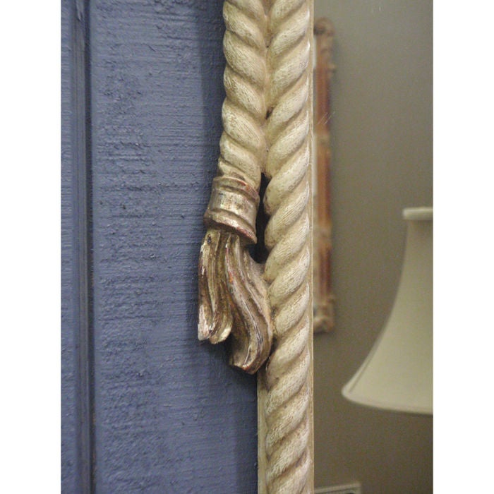 This playful rope and tassel design mirror is all hand-carved and silver parcel-gilt with an aged white patina. It has the playful tromp l'oiel that Fornasetti would have loved, as it appears to be hanging from the bow. The mirror still has the